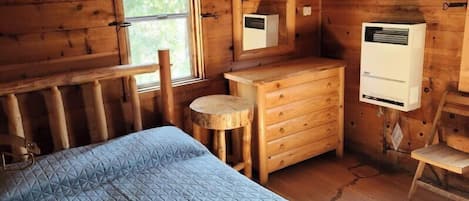 Quarto de cabana de madeira com uma cama, cômoda, mesa pequena e janela.