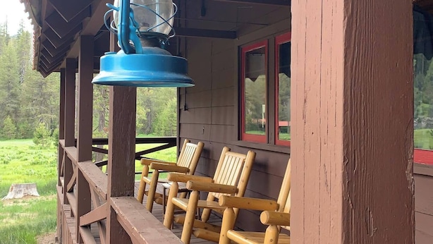 Une véranda en bois, ornée d’une lanterne bleue suspendue au plafond, de chaises en bois et offrant une vue sur un paysage verdoyant.