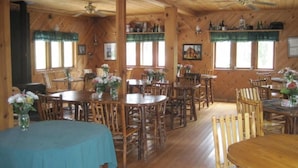 Une cabane en bois dotée de plusieurs tables et chaises, de grandes fenêtres et d’un ventilateur de plafond.