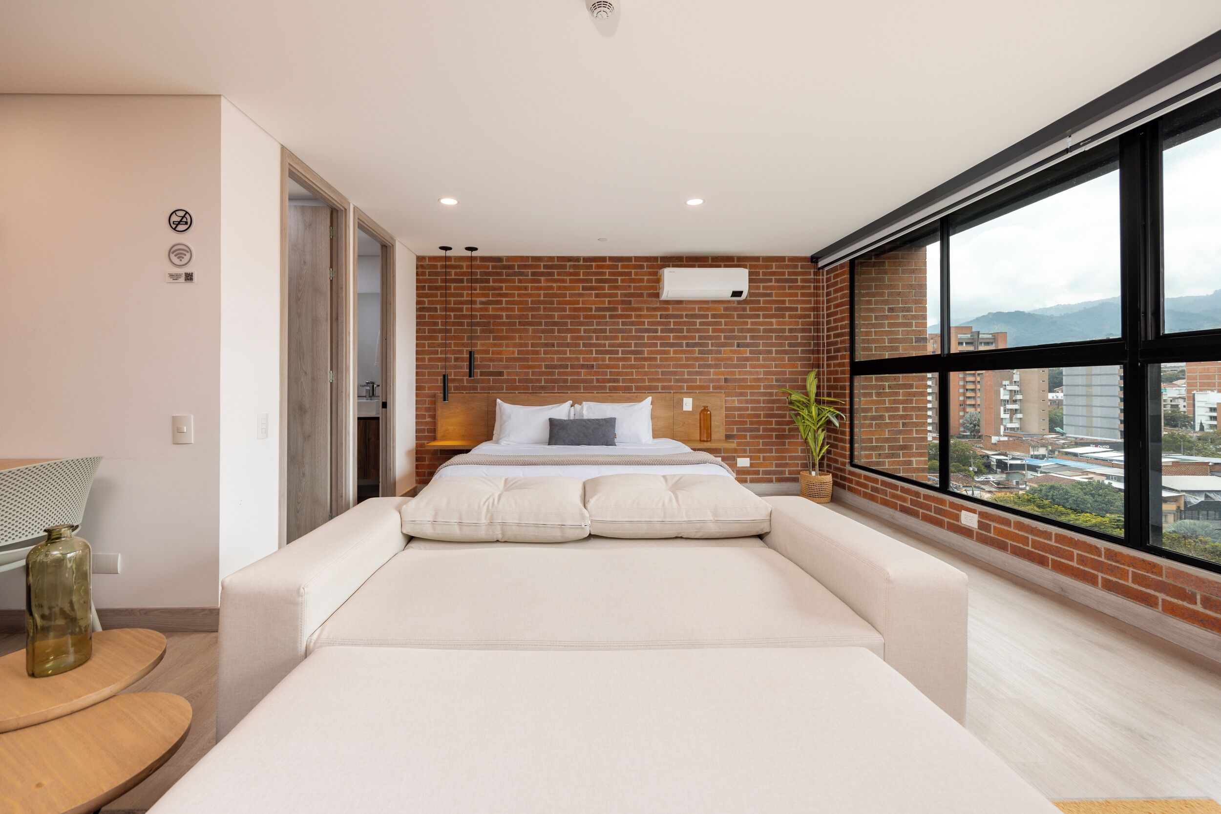 A modern bedroom with a brick wall, a large window, and a bed with white bedding.
