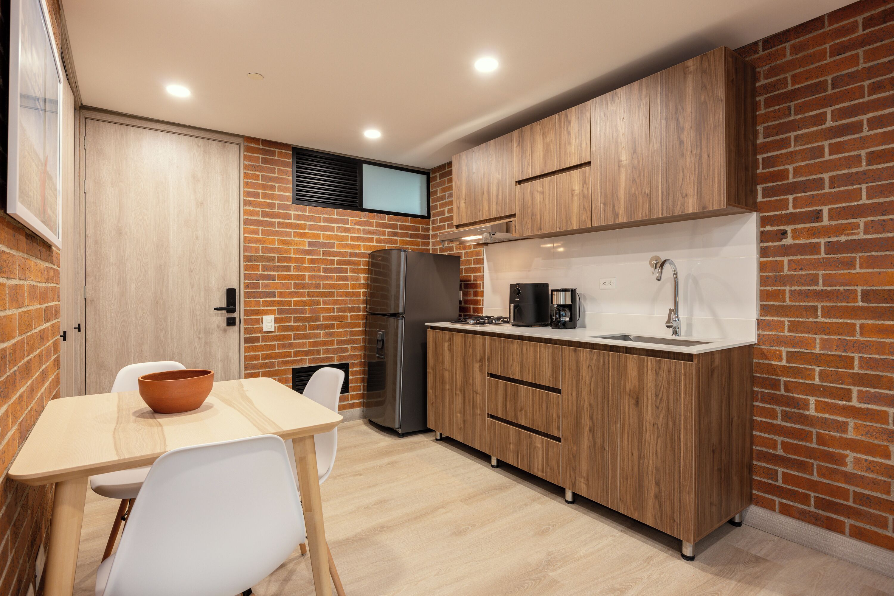 A compact kitchen with wooden cabinets, a refrigerator, a sink, and a white countertop.