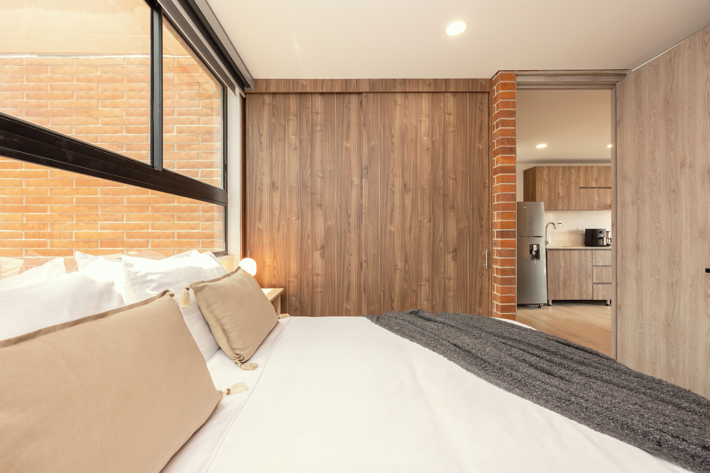 Une chambre moderne avec un grand lit, une vue sur la cuisine et un mur en briques.