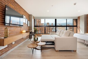 Una sala de estar moderna con pared de ladrillo, un ventanal grande, un sofá, una mesa de centro y un televisor montado en la pared.