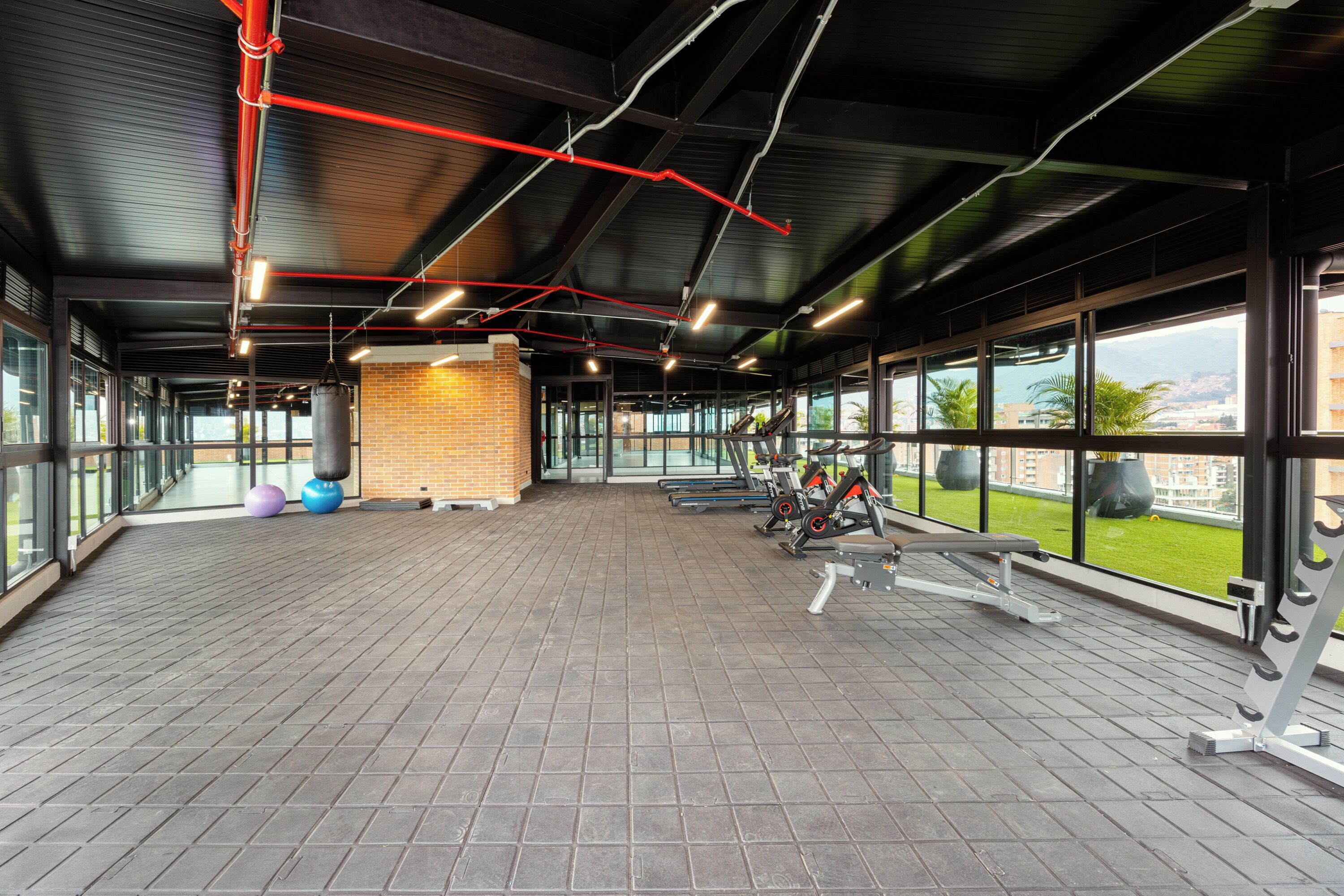 A spacious gym with exercise equipment, large windows, and a brick wall.