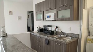 A modern kitchen with granite countertops, stainless steel appliances, and wooden cabinets. - Three room apartment (Cancún)