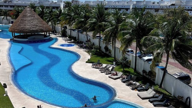 A resort pool with a winding design, lounge chairs, and palm trees. - Three room apartment (Cancún)