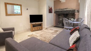 A living room with a sofa, TV, fireplace, and dining area. - Tryfan Cottage (Caernarfon)