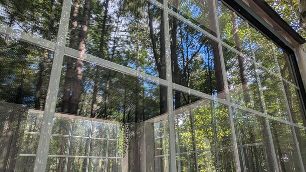 A room with large windows offering a view of a forested area. - Little Can in the Pines - Bunkie No. 1 (SIMCOE)