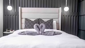 Un dormitorio moderno con una cama blanca, dos almohadas con estampado blanco y negro, y una original disposición de toallas.