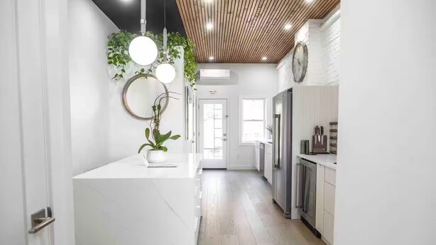 Una cocina moderna con armarios blancos, una isla central con una planta e iluminación colgante.