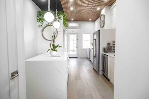 A modern kitchen with white cabinetry, a central island with a plant, and pendant lighting. - Miami styled living - Min to NYC (Edgewater)