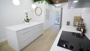 Una cocina moderna con armarios blancos, una cocina por inducción negra y una pequeña orquídea en maceta.