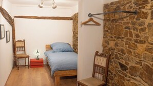 Une chambre à coucher avec un lit en bois, une chaise, une table de chevet avec une lampe et un mur en pierre.