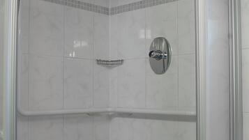 Une douche fermée par des parois en verre, dotée d’un pommeau de douche à main, d’un siège intégré et d’une petite étagère.