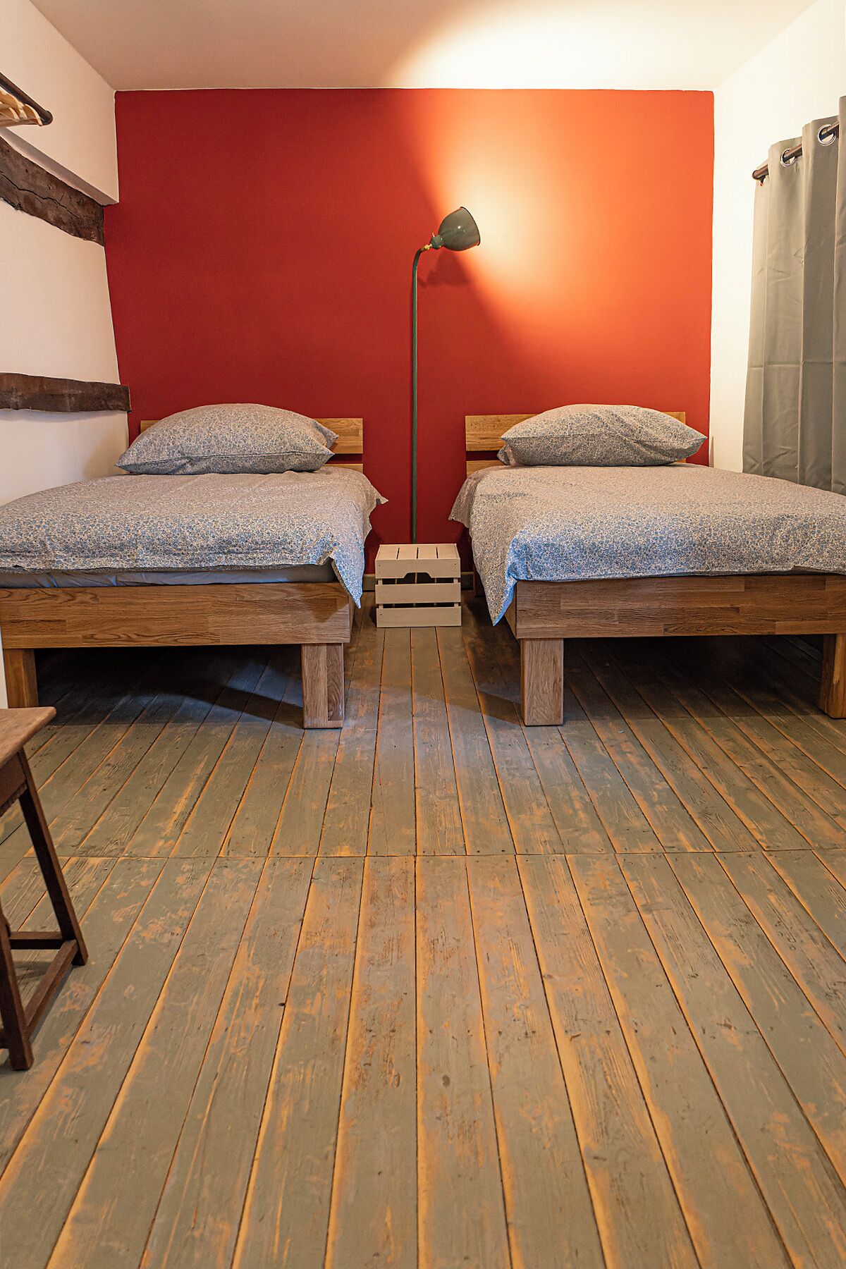 Une pièce avec deux lits en bois, un mur rouge et un plancher en bois.