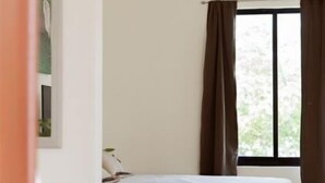 A bedroom with a bed, a window with curtains, a small table, and a wall-mounted shelf. - Saules Sueño (Cancún)
