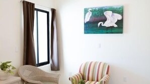 A modern living room with a ceiling fan, a window with curtains, a striped armchair, a white sofa, and a painting of birds. - Saules Sueño (Cancún)
