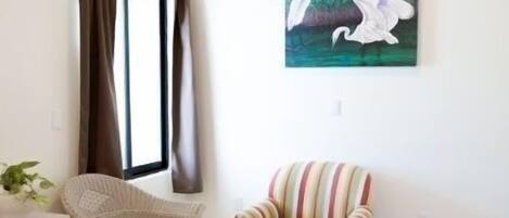 A modern living room with a ceiling fan, a window with curtains, a striped armchair, a white sofa, and a painting of birds.