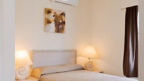 A hotel room with a bed, two bedside lamps, an air conditioning unit, and a wall-mounted artwork. - Saules Sueño (Cancún)