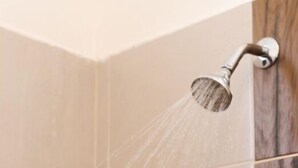 A shower with water running, a wooden panel on the wall, and beige tiles. - Saules Sueño (Cancún)