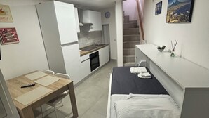 A compact room with a bed, a small table, a kitchenette, and a staircase leading to another level. - HOUSE OF TOTONN (Unknown)
