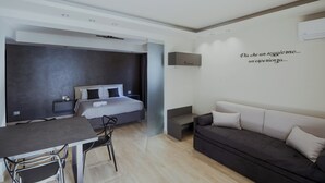 A modern hotel room with a bed, a sofa, a dining table, and a small seating area. - APARTMENT 1 (Misterbianco)
