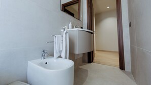 A modern bathroom with a white sink, mirror, and wooden door. - APARTMENT 2 (Misterbianco)