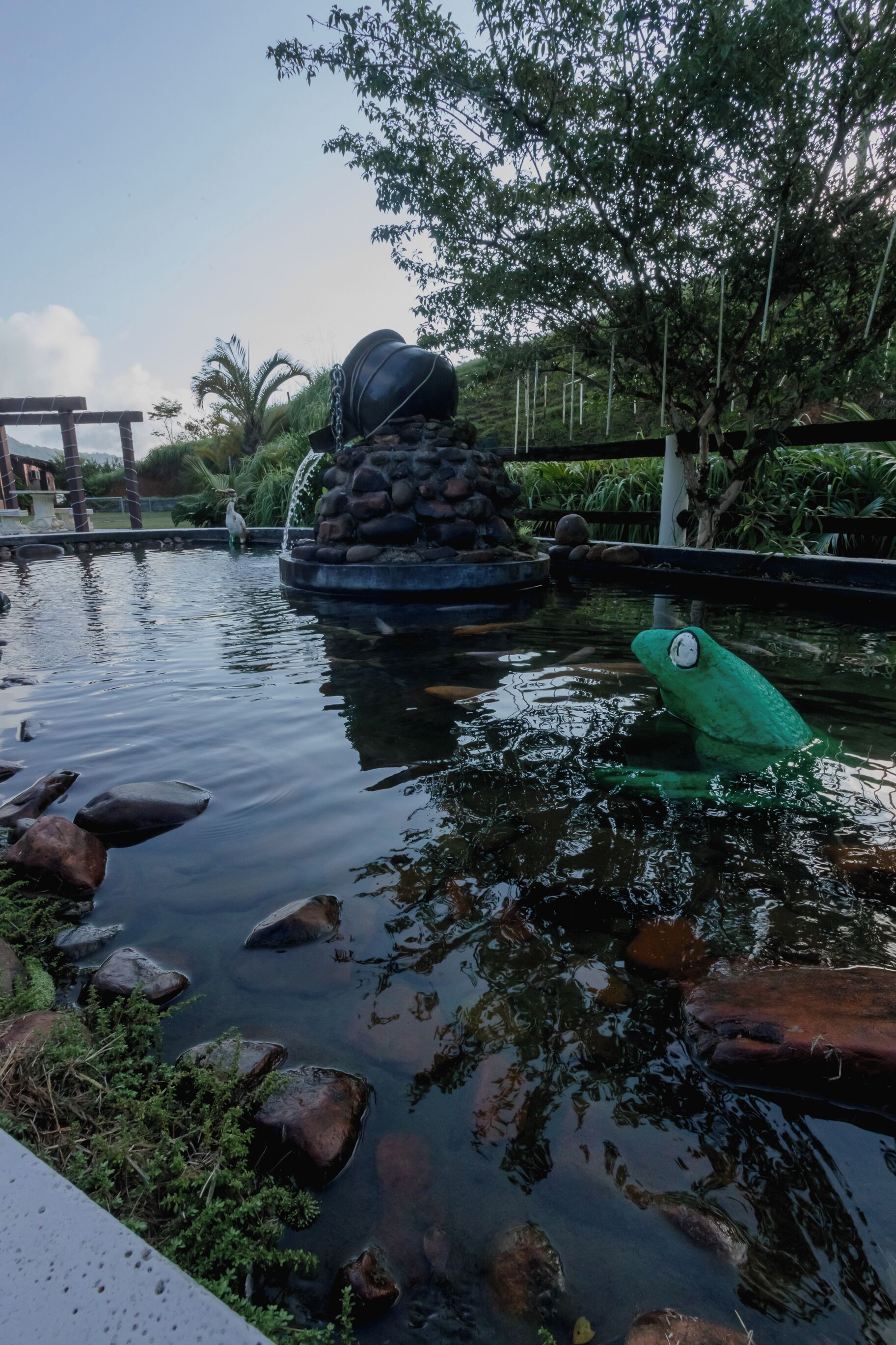 A pond with a fountain, surrounded by rocks and greenery.