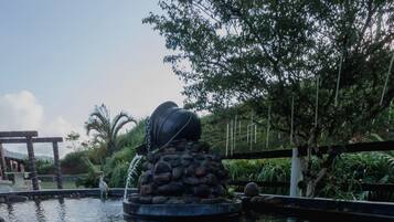 A pond with a fountain, surrounded by rocks and greenery.