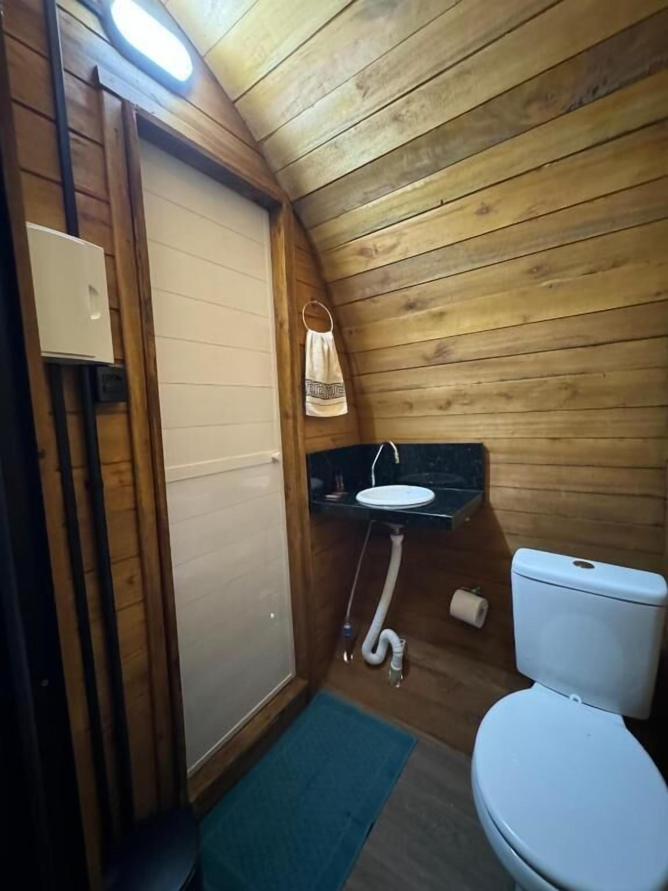 Ein kleines Badezimmer mit Holzvertäfelung, ausgestattet mit Toilette, Waschbecken und Duschbereich.