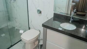 A modern bathroom with a glass shower enclosure, a white toilet, a sink with a mirror, and a small window.