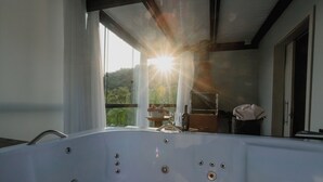 A modern bathroom with a large bathtub, a view of the outdoors, and a window with curtains. - Recanto Fogo na Taça (Jaraguá do Sul)
