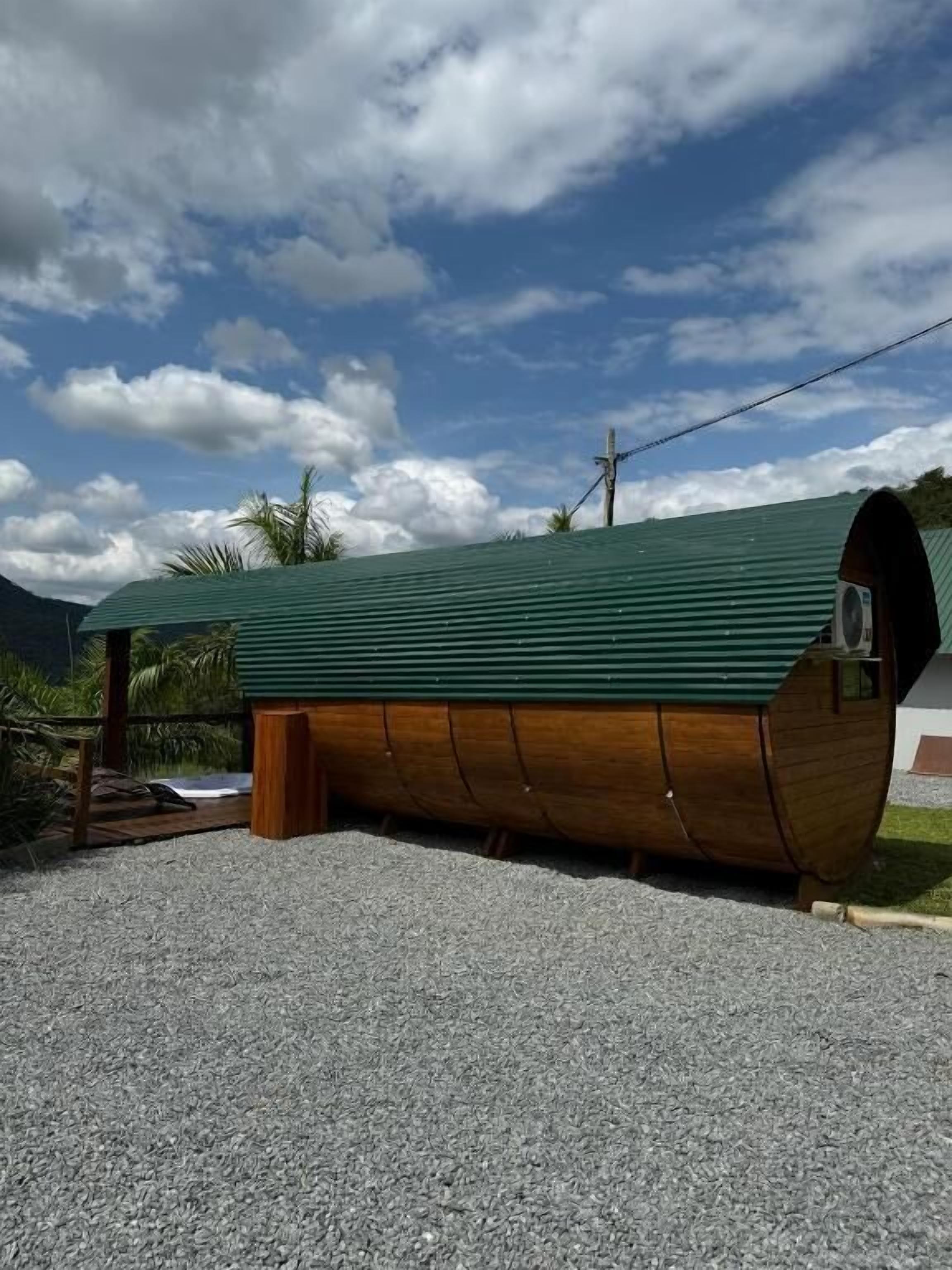 A wooden boat-shaped building with a green roof, situated on a gravel surface with a clear sky and mountains in the background.