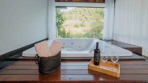 A hot tub with a bottle of wine and glasses on a wooden deck, with a view of greenery outside. - Recanto Fogo na Taça (Jaraguá do Sul)