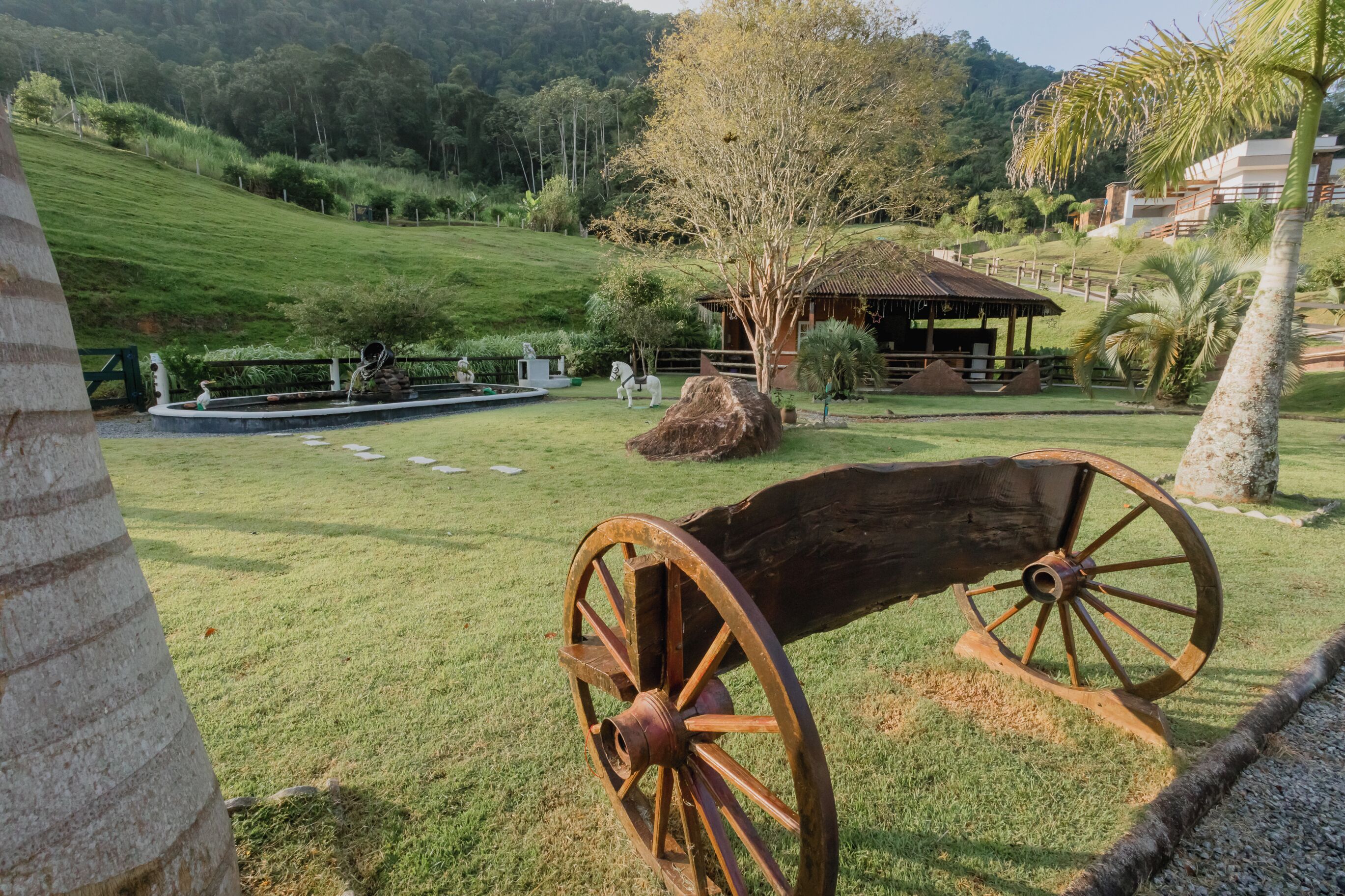 A grassy area with a large wooden cart, a small building, and a tree.