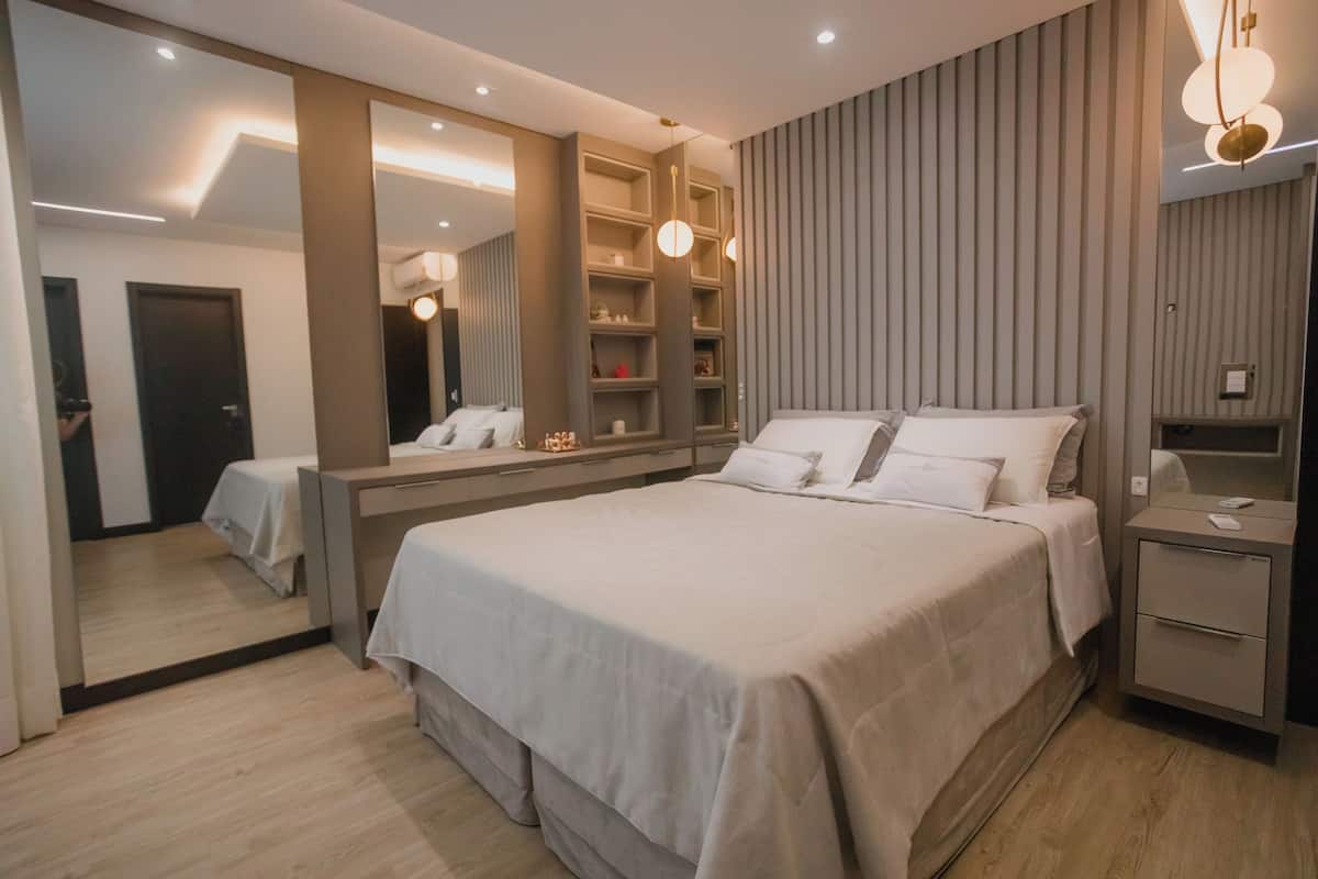 A modern bedroom with a large bed, a bedside table, a mirror, and built-in shelving with decorative items.