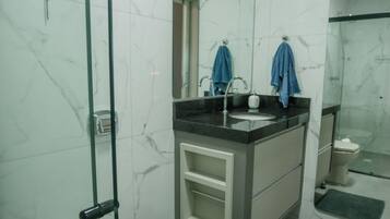 Un baño con inodoro, lavamanos, espejo y zona de ducha.