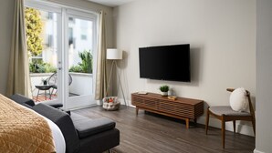 A modern hotel room with a large bed, a flat-screen TV, a wooden side table, a chair, and a view of the outdoors. - Tangerine Terrace - 10 min to Disney/Angel Stadium (Orange)
