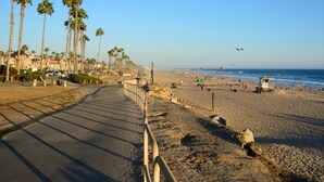 A beach with a paved walkway, palm trees, and a lifeguard tower. - Casa Clementine - 10 min to SNA/Beach+Free Parking (Orange)