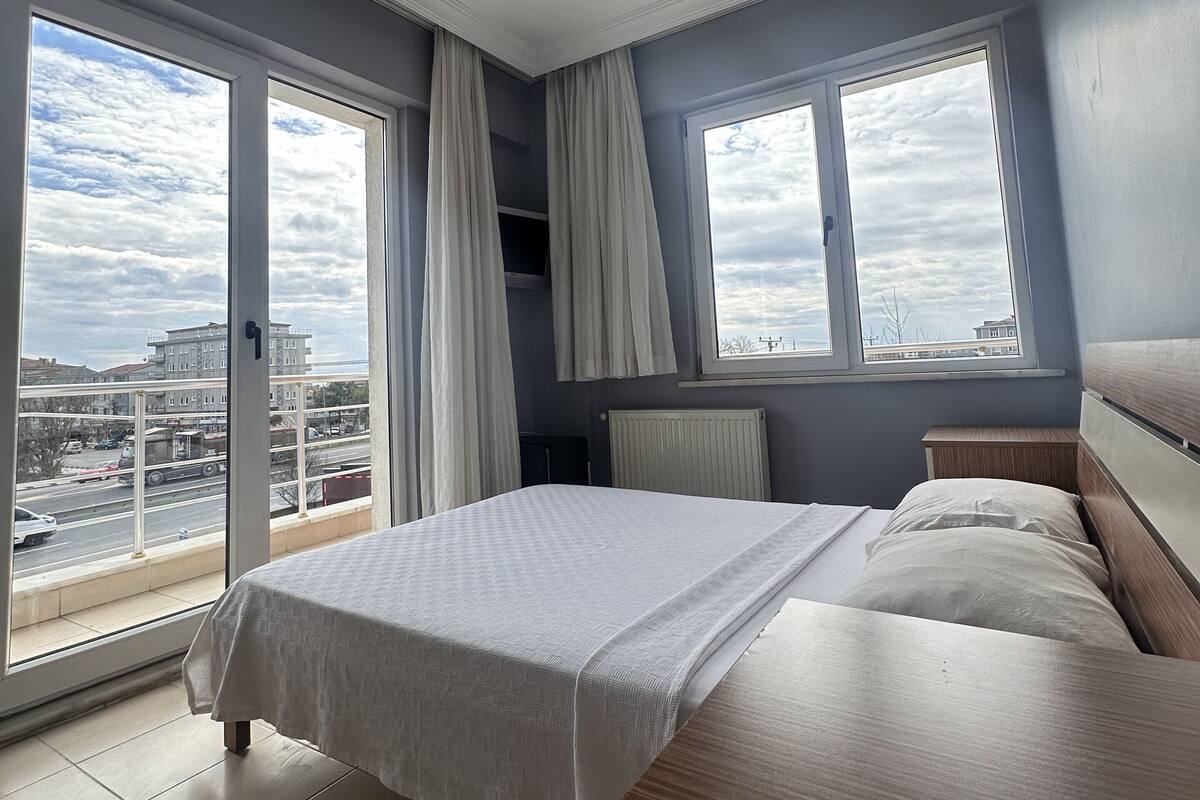 Un dormitorio con una cama grande, una mesita de noche de madera, una ventana con cortinas y vistas a la ciudad.