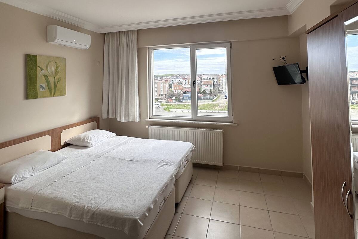 Habitación de hotel con una cama grande, una ventana con vista a la ciudad, un radiador y un televisor de pantalla plana montado en la pared.