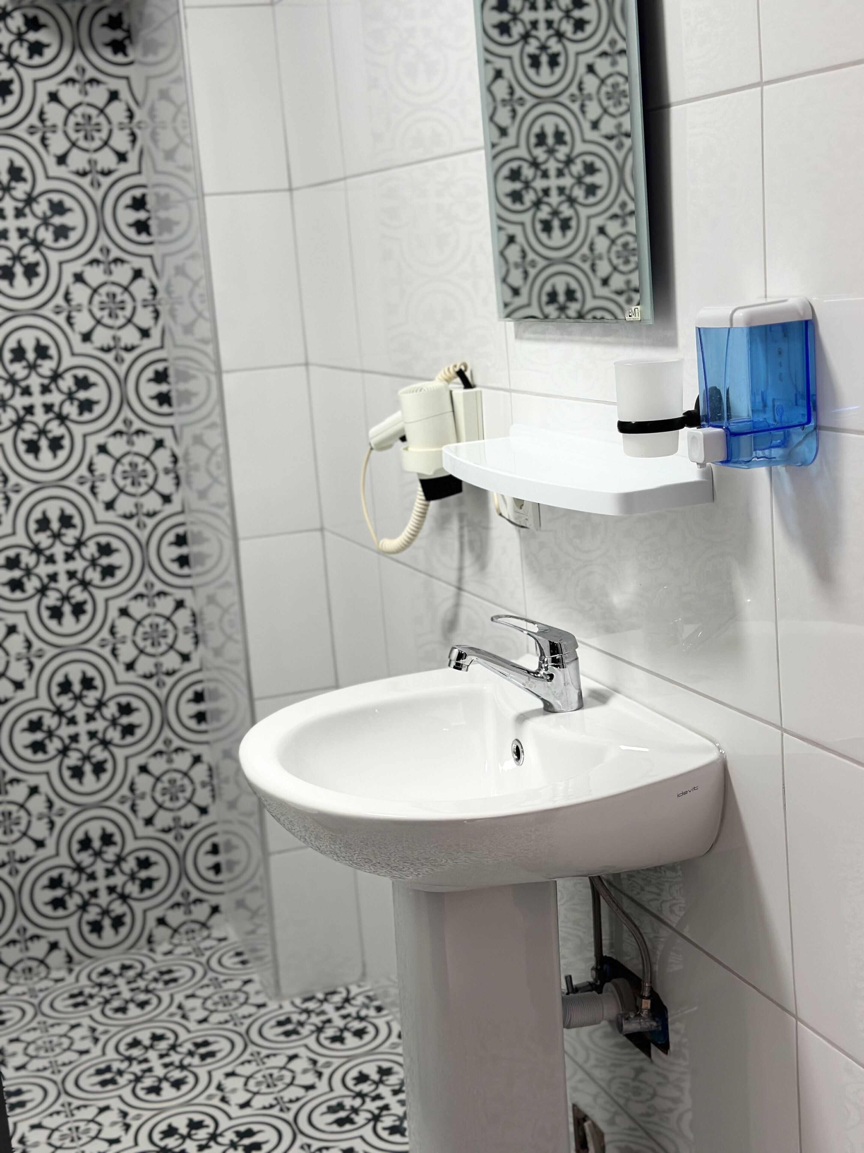 A bathroom with a white sink, a mirror, and a patterned tile backsplash.