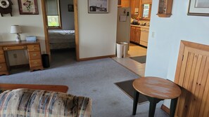 A room with a bed, a desk, a chair, a radiator, a window, and a kitchen visible through an open door. - Thisldu for Your Summer Vacation! Private Dock! (Ferrisburgh)