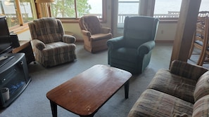A living room with a view of the water, furnished with a sofa, two armchairs, and a coffee table.
