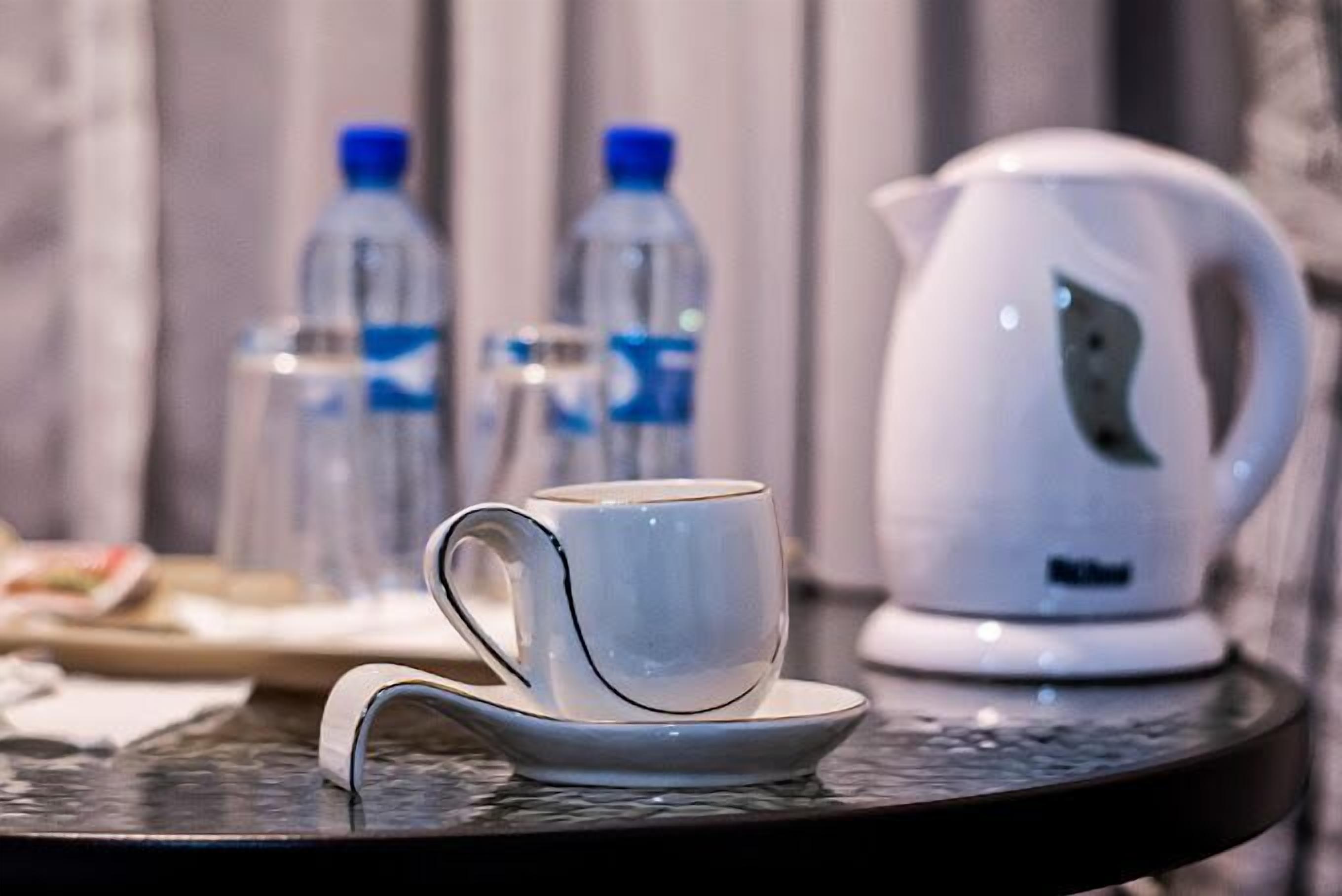 A white mug on a saucer, a white electric kettle, and two water bottles on a table.