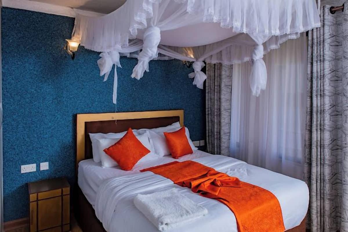 A hotel room with a bed, white bedding, orange pillows, a white canopy, and a blue textured wall.