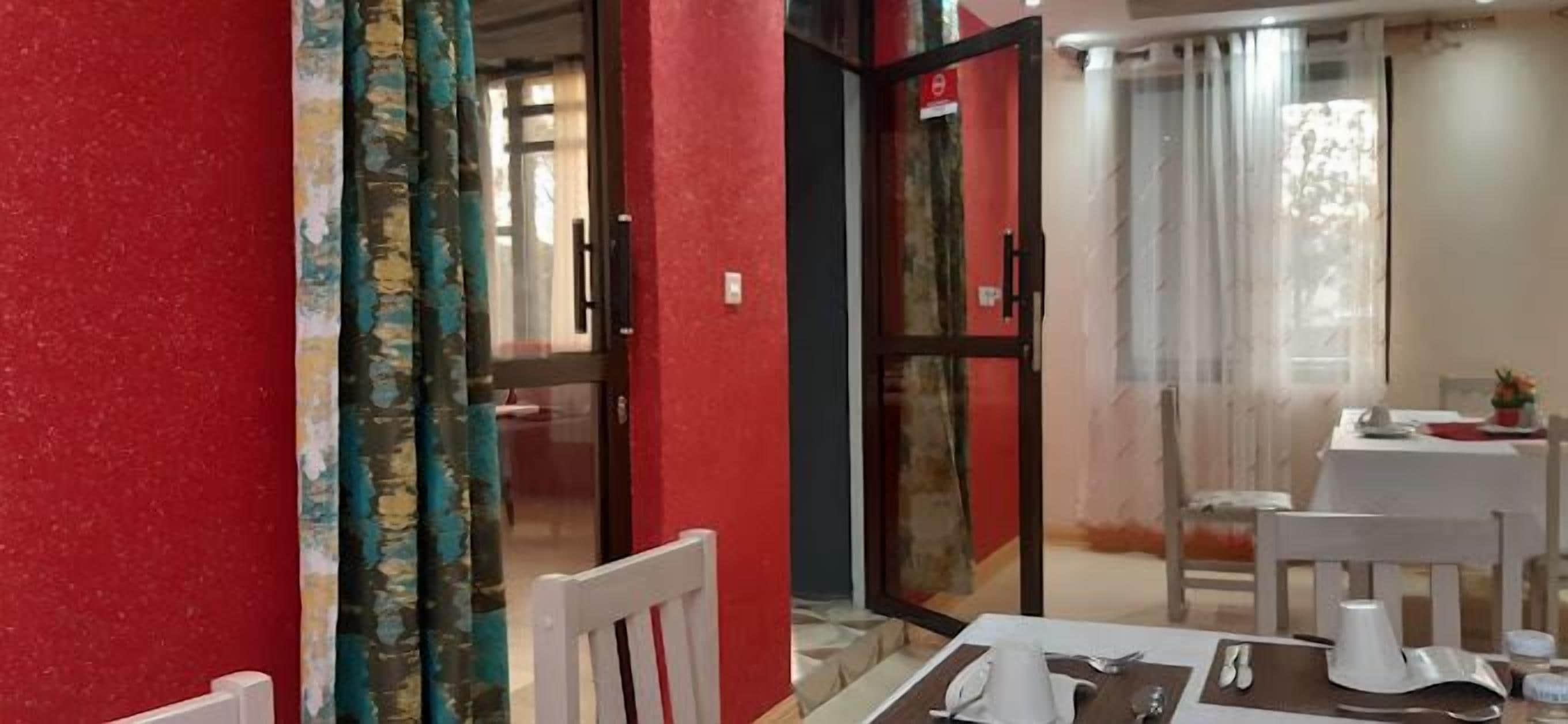 A dining area with a table set for two, a red wall, and a door leading to another room.
