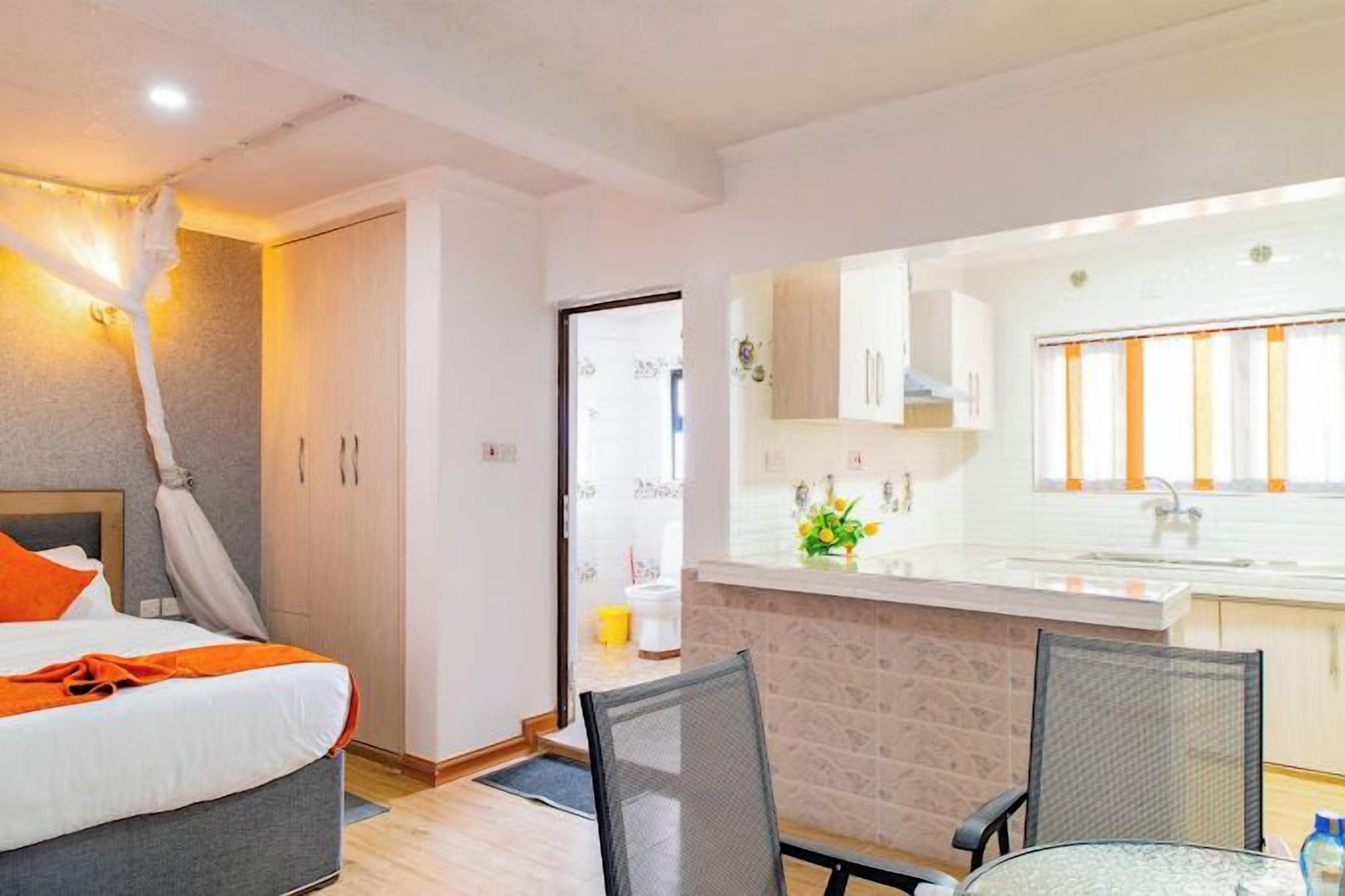 Een hotelkamer met een bed, een eettafel met stoelen, een kitchenette en een badkamer die door een open deur zichtbaar is.
