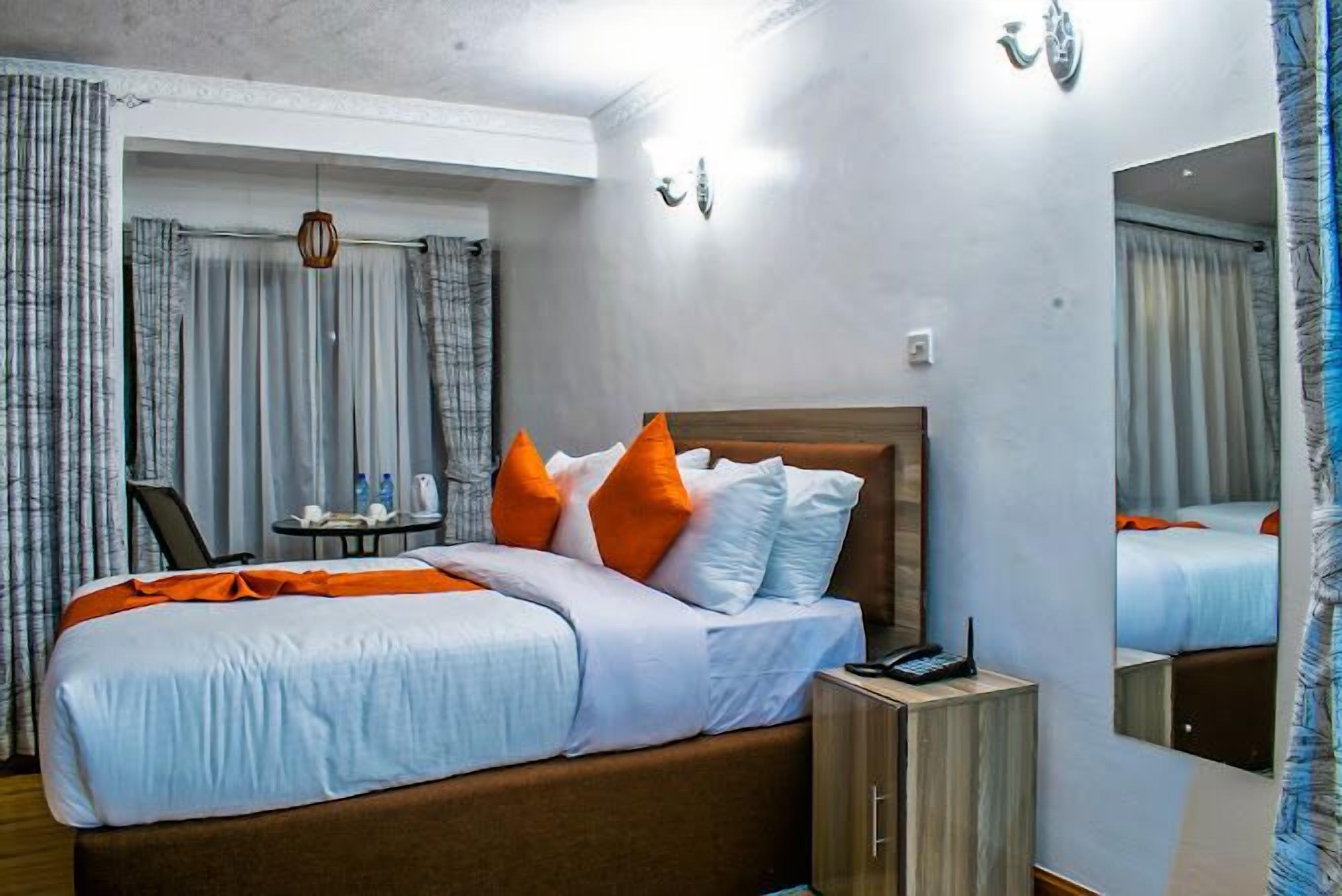A hotel room with a bed, a bedside table, a mirror, and curtains.