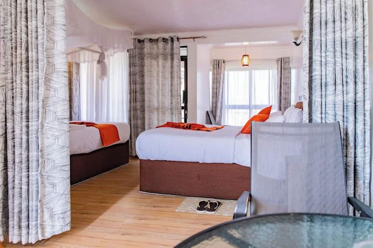 A hotel room with two beds, a sitting area, and a view of the outdoors.